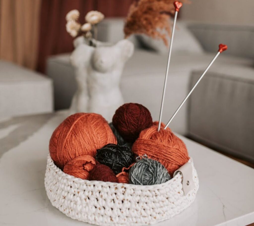 Aesthetic arrangement of yarn balls in a crochet basket with knitting needles for a cozy crafting ambiance.